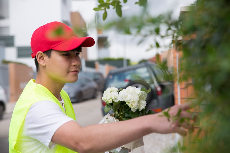 A young male delivery person wearing a red cap and a high-visibility yellow vest is shown delivering a floral gift. He is holding a bouquet of fresh white hydrangeas with green leaves, arranged neatly