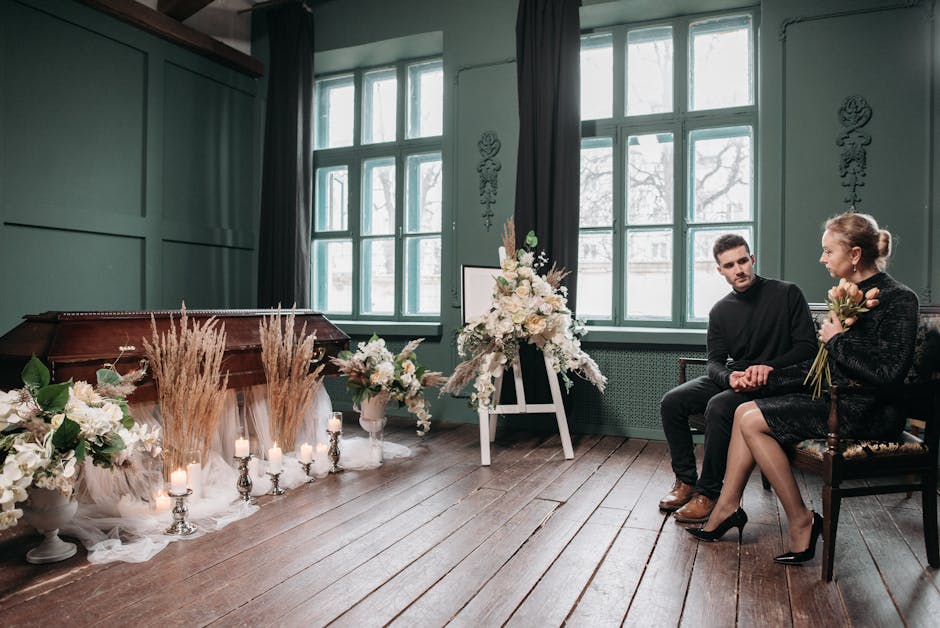 A woman hands a bouquet of peach and cream roses, white peonies, and greenery to a young man in a black sweater, both seated on a vintage wooden chair in a softly lit, vintage-style room with teal wal